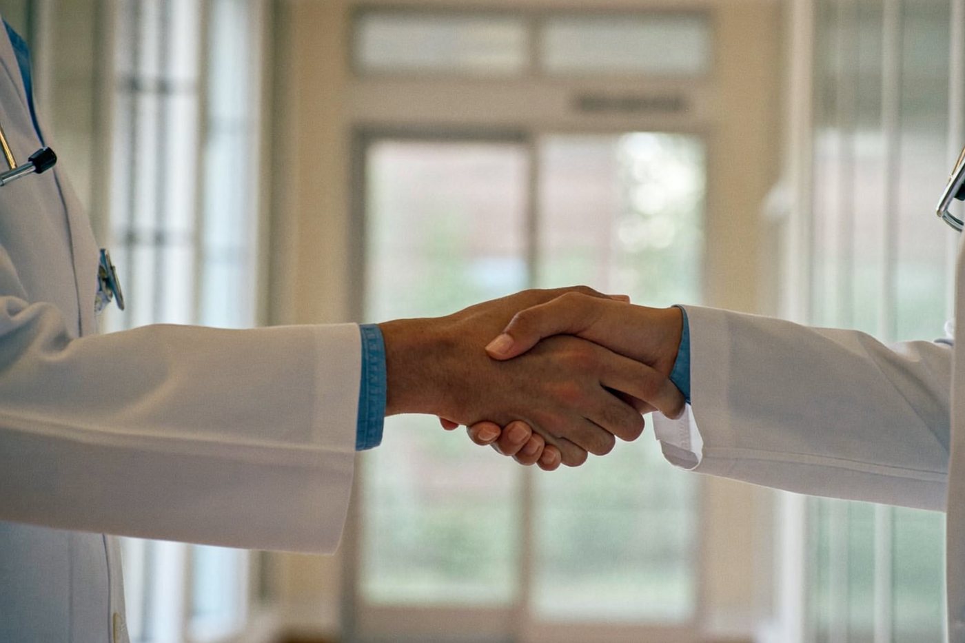 Handschlag zwischen zwei Ärzten in einem hellen Klinikflur